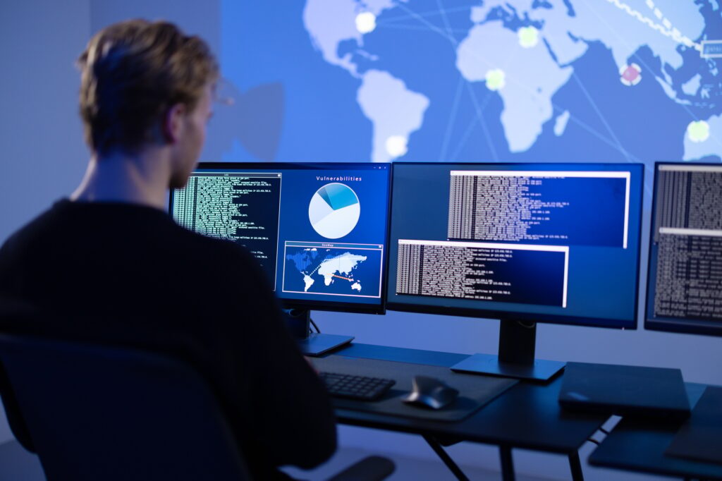 Back View in the Cyber Security Control Center Operator Working. Multiple Screens Showing Technical